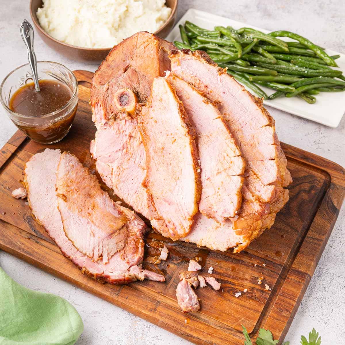 Slice coke glazed ham on a cutting board with juices spooned over the top.
