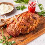 A Coca-Cola brown sugar and mustard glazed ham on a cutting board.