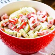 A large red serving bowl filled with creamy cucumber and tomato salad