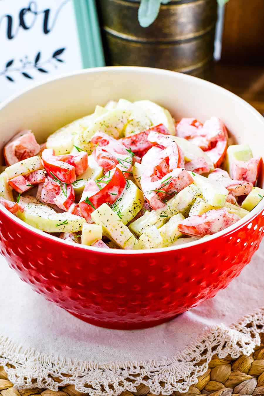 A large red serving bowl filled with creamy cucumber and tomato salad