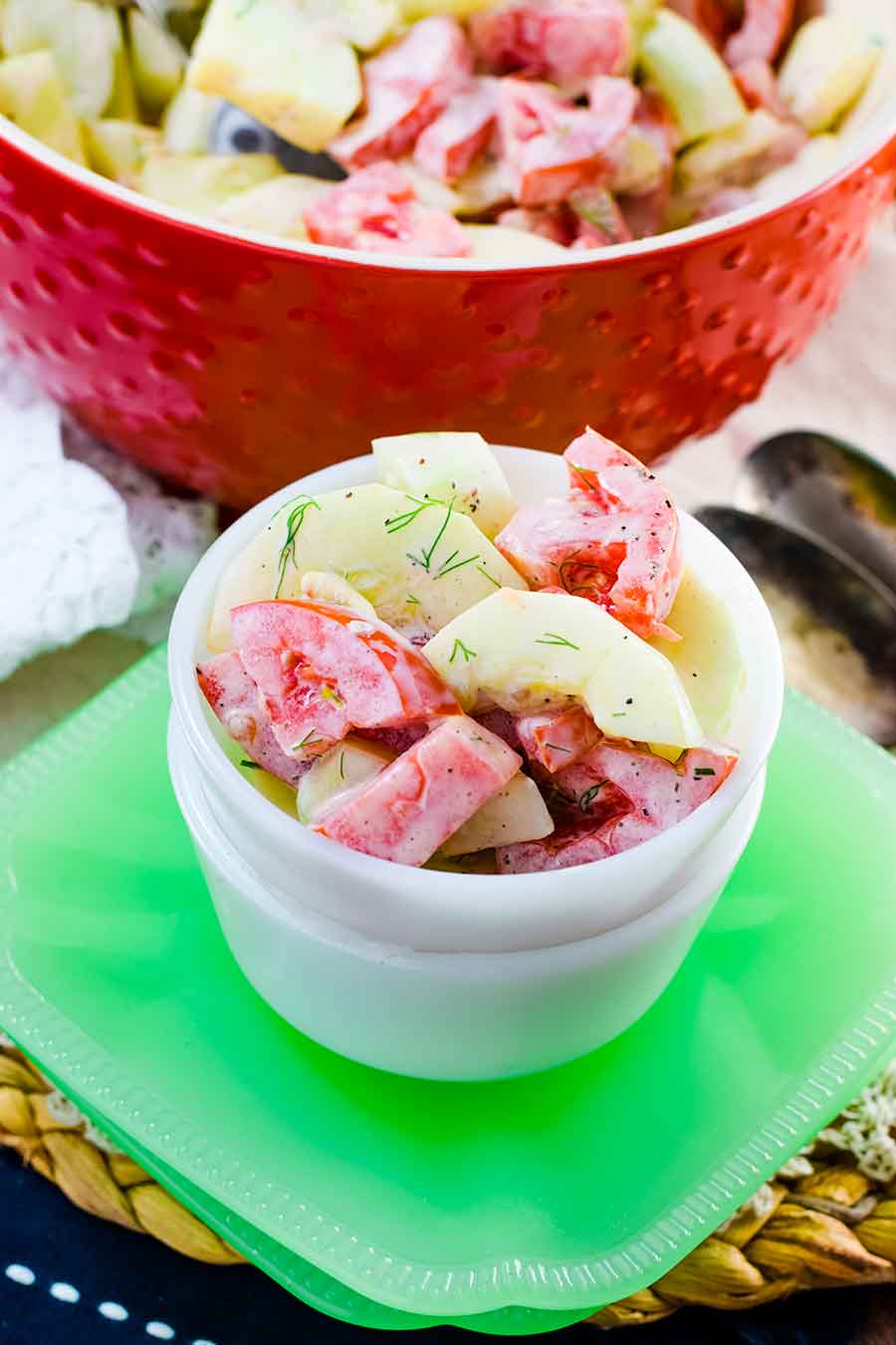 A small white bowl of creamy cucumber and tomato salad on a green napkin