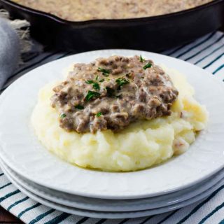 A white plate filled with mashed potatoes that are topped with this easy creamed hamburger gravy recipe