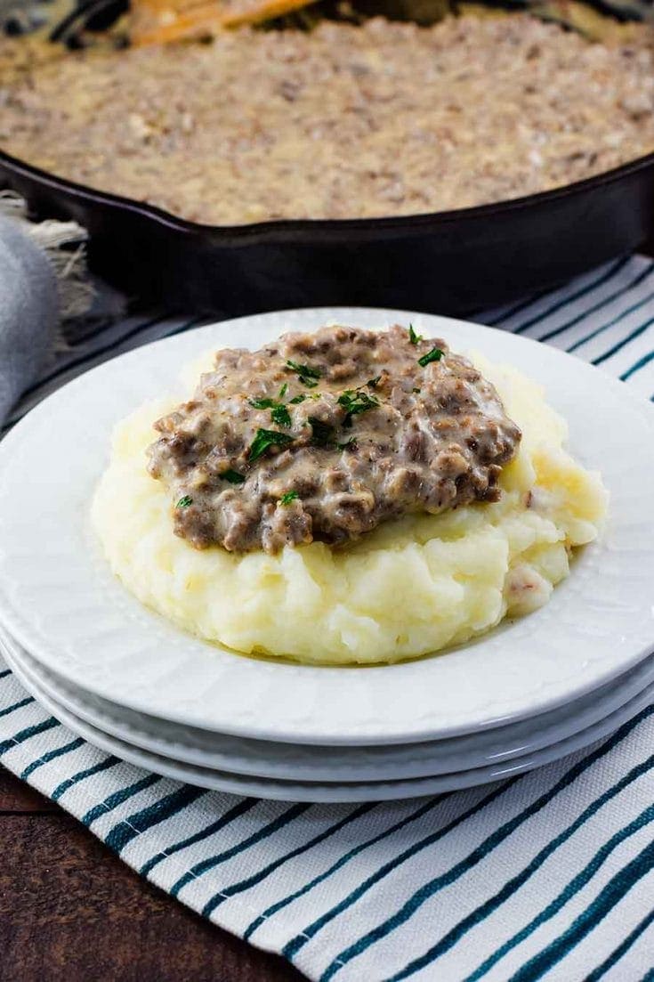 A white plate filled with mashed potatoes that are topped with this easy creamed hamburger gravy recipe