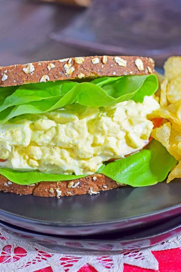 A Classic Egg Salad Sandwich served on two slices of wheat bread with lettuce and potato chips