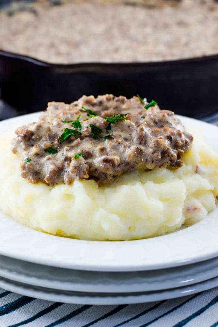 A white plate filled with mashed potatoes that are topped with this easy creamed hamburger gravy recipe