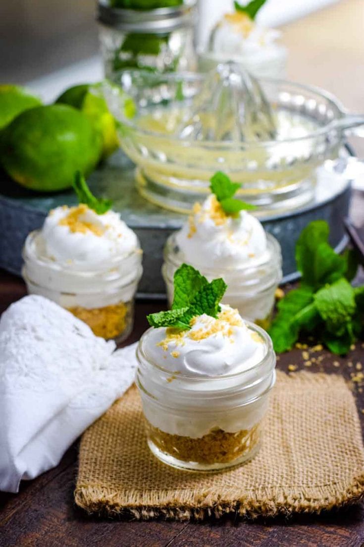 A table set with burlap and embroidered white napkin with key lime pie in a jar displayed.