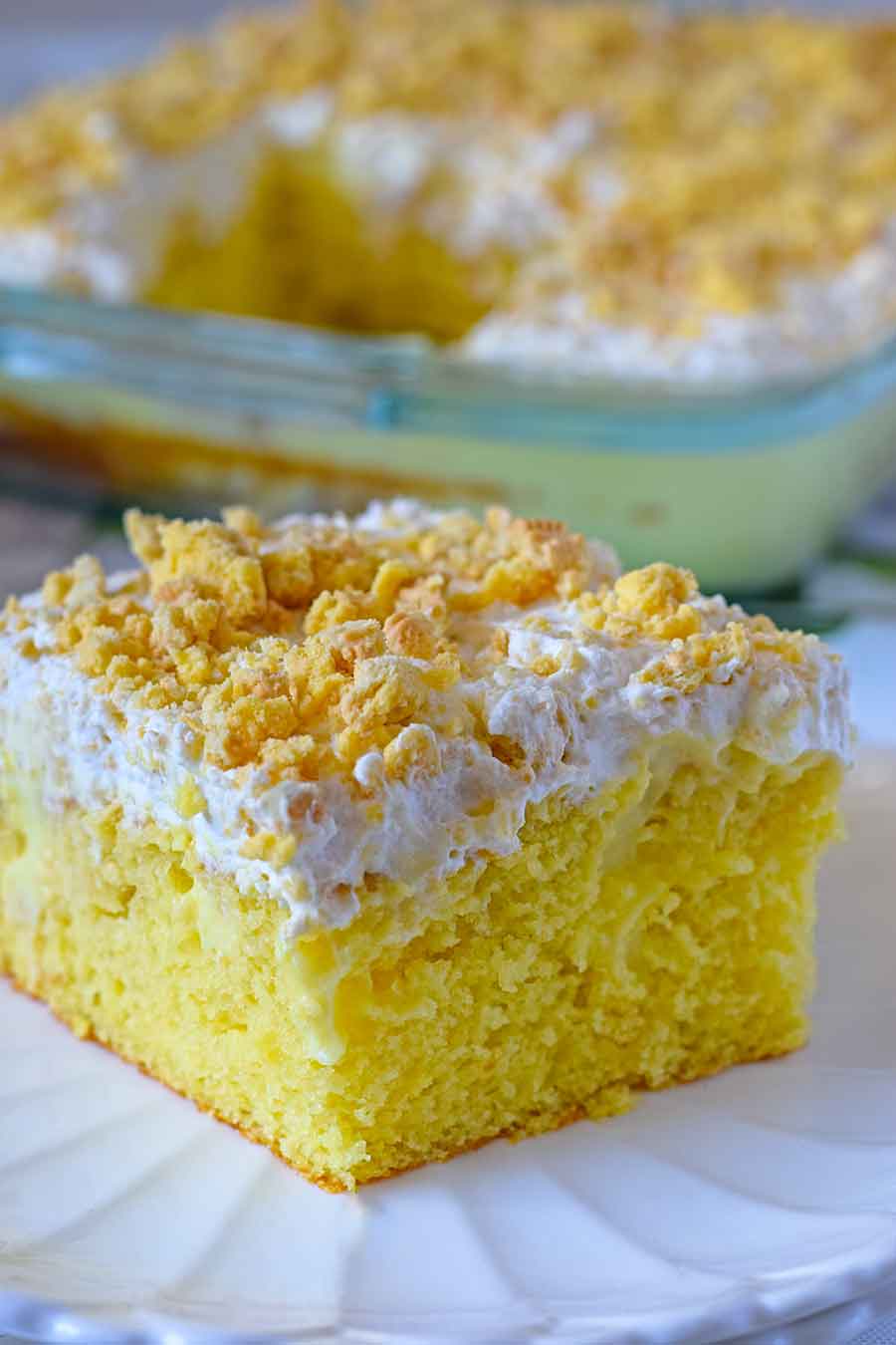 A slice of lemon cake topped with whipped icing on a white plate.