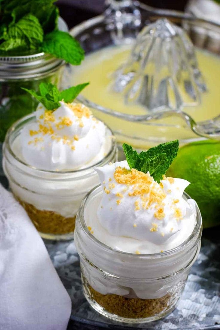 Key lime pie jars on tin cake server with lime juicer in background.