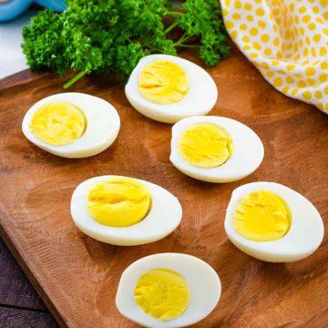 Perfect Instant Pot Boiled Eggs sliced in half to reveal yellow yolks and egg whites on top of a wooden cutting board with parsley in the background