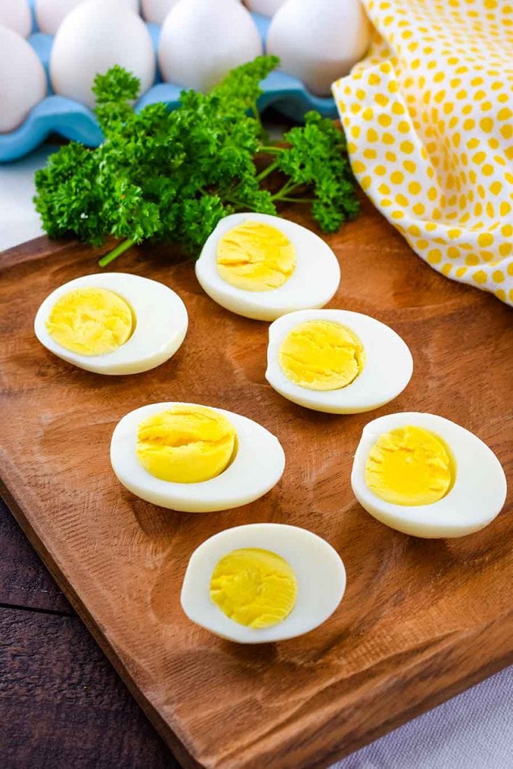 Perfect Instant Pot Boiled Eggs sliced in half to reveal yellow yolks and egg whites on top of a wooden cutting board with parsley in the background
