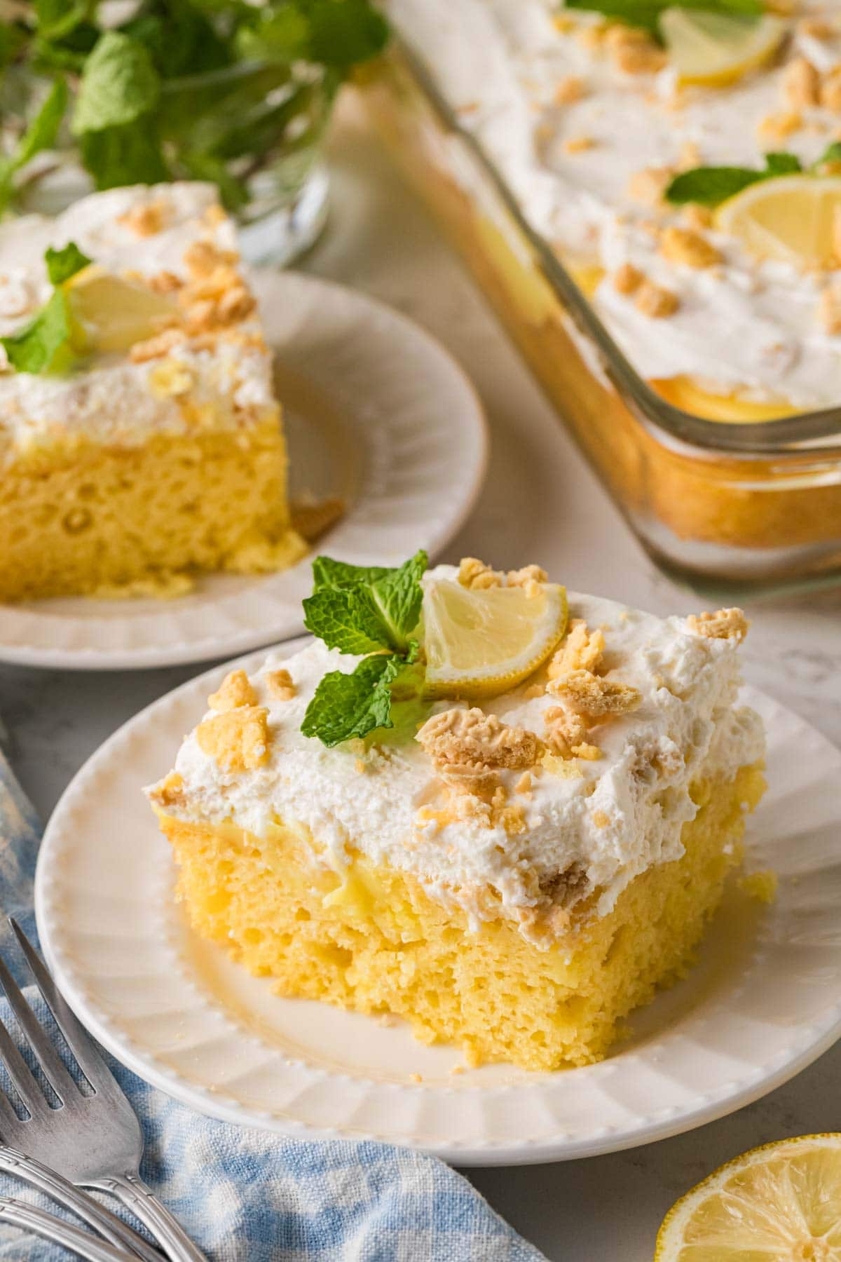 A slice of lemon poke cake topped with whipped cream icing and crushed lemon cookies.