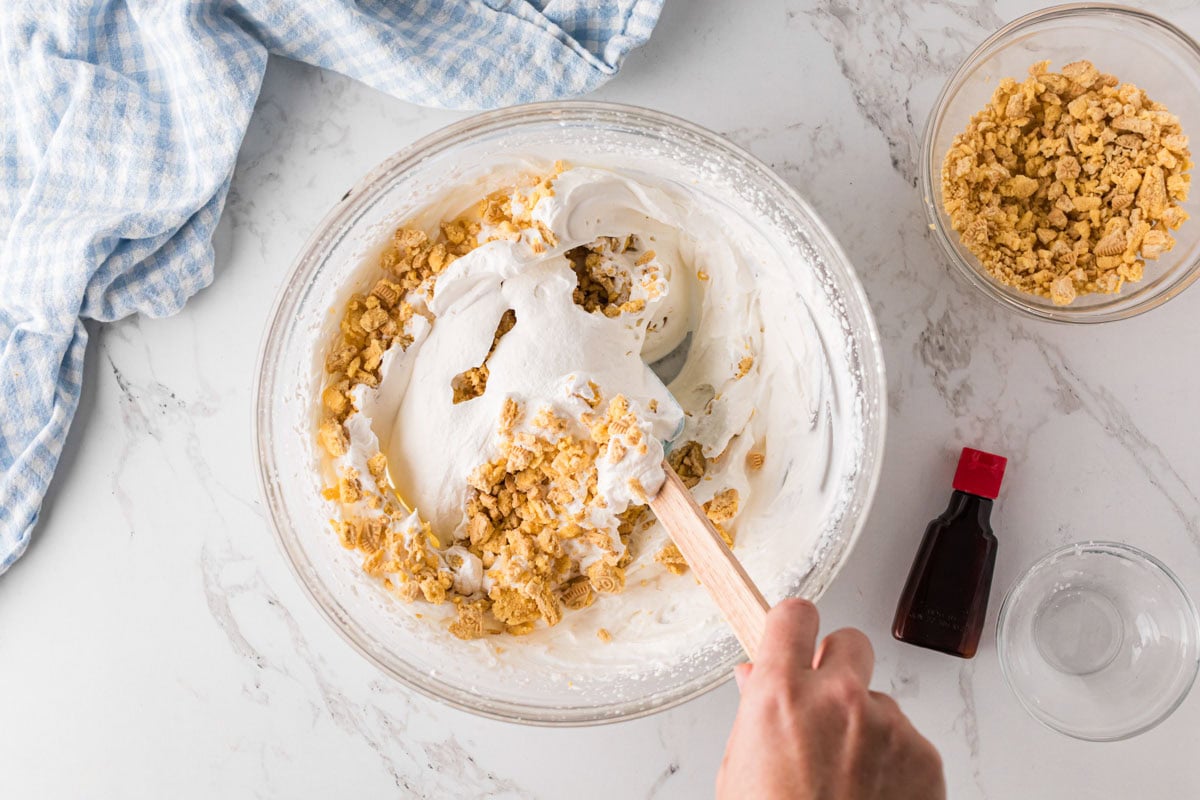 Folding cookie crumbs into whipped cream in a bowl.