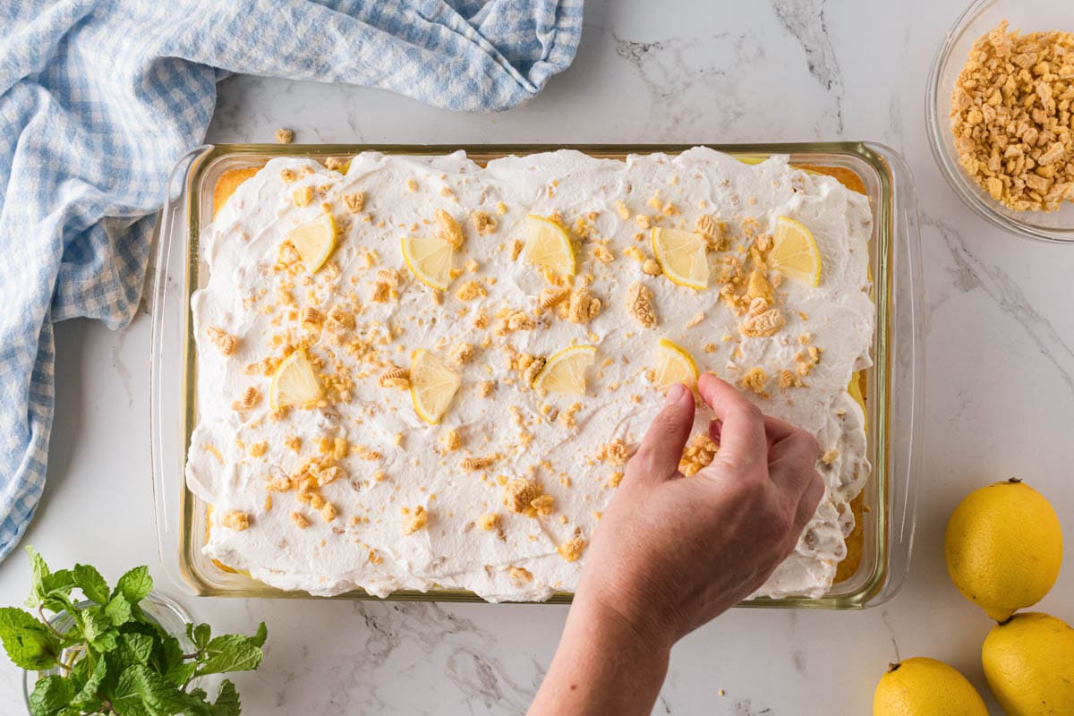 Adding chopped cookies on top of whipped icing on the lemon pudding cake.