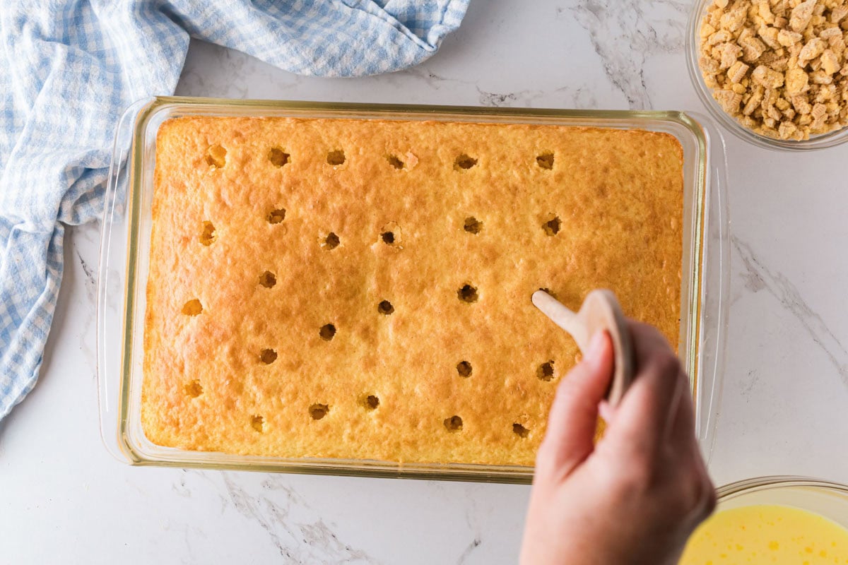 Using the back of a wooden spoon to poke holes in the lemon cake after baking.