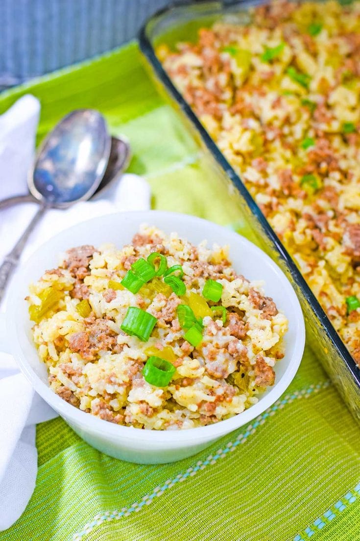 a white bowl filled with ground beef and sausage casserole garnished with green onion slices and a silver spoon on the side