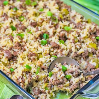 a casserole dish filled with beef and sausage rice casserole and a serving spoon