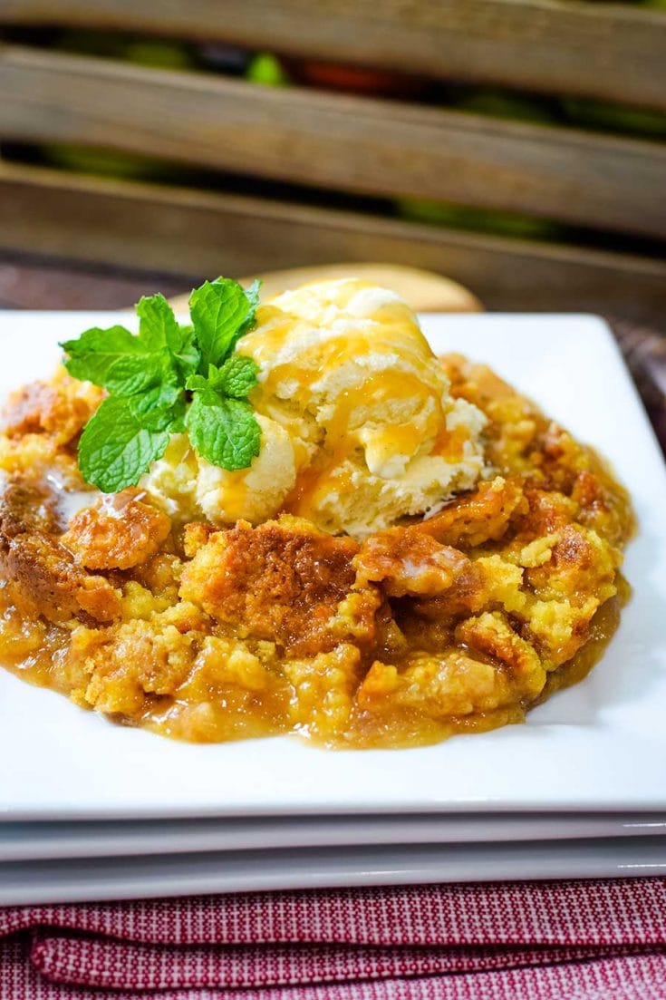 a serving of this caramel apple dump cake with fresh mint, vanilla ice cream, and caramel sauce on a white plate