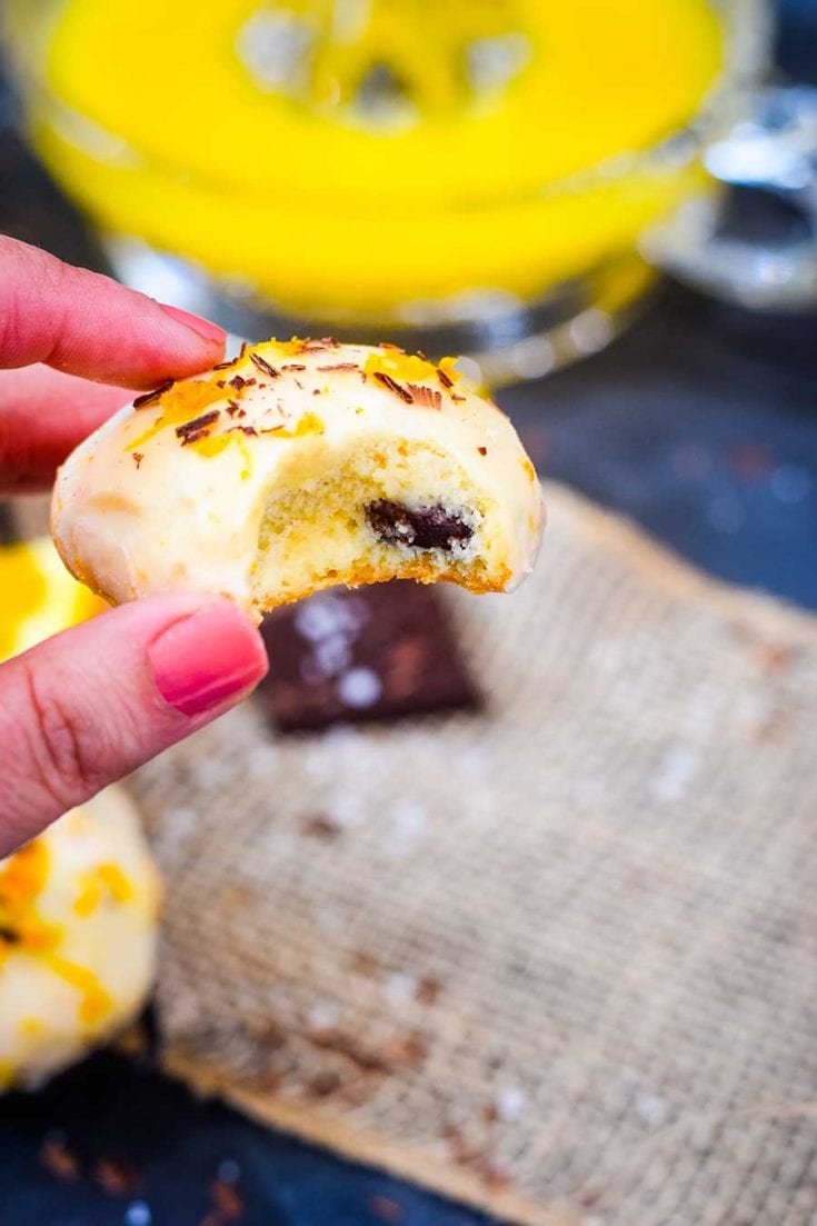 A hand holding up a salted dark chocolate orange cookie with a bite taken out of it