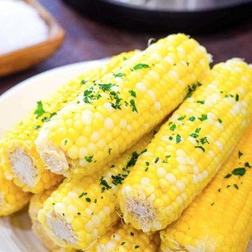 Instant Pot buttered corn on the cob sprinkled with parsley on a white plate