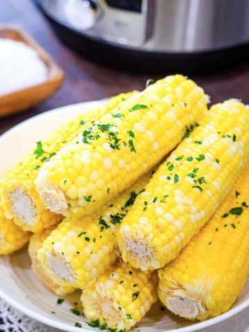 Instant Pot buttered corn on the cob sprinkled with parsley on a white plate