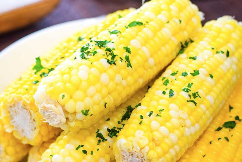 Instant Pot buttered corn on the cob sprinkled with parsley on a white plate