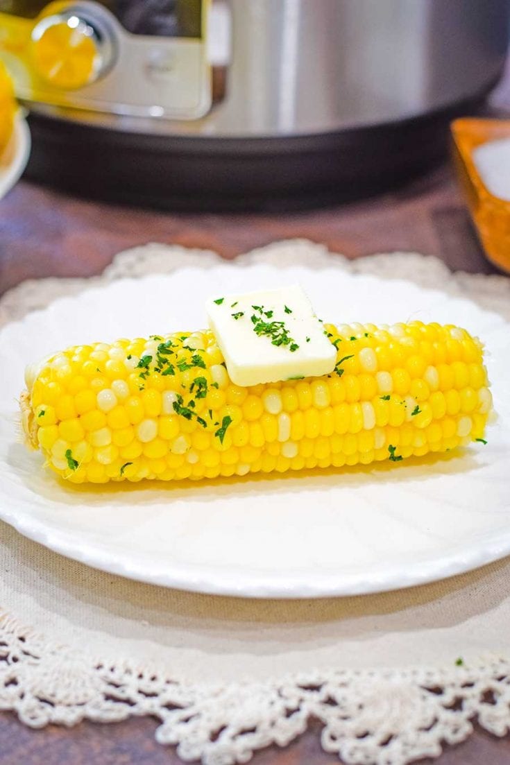 Instant Pot Corn on the Cob on a white plate with a pad of butter and chopped parsley