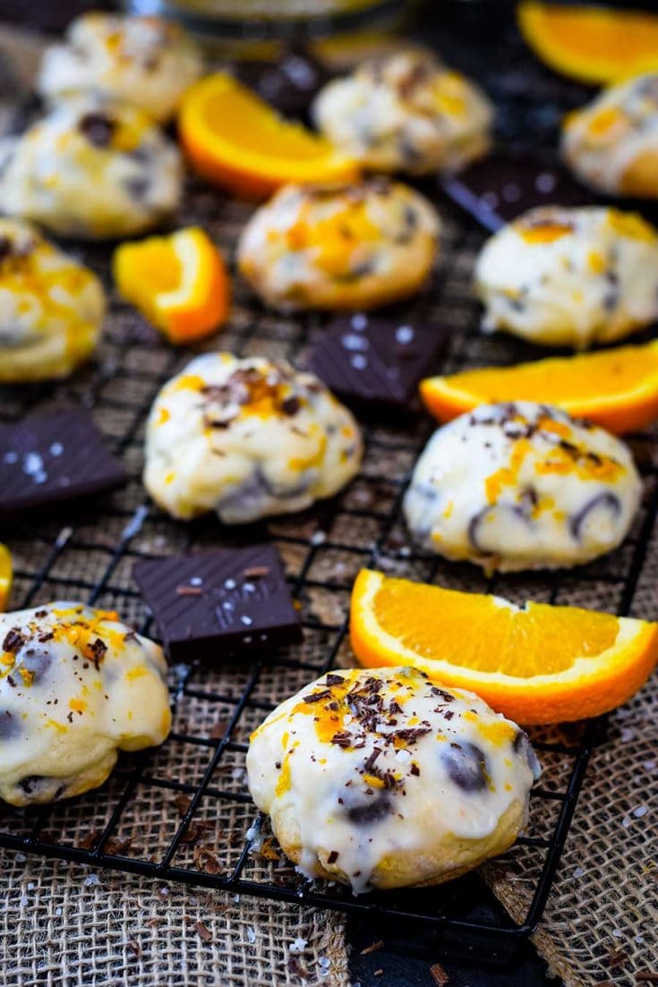 An up-close of salted dark chocolate cookies on a cooling rack with sliced oranges and chocolate garnish.