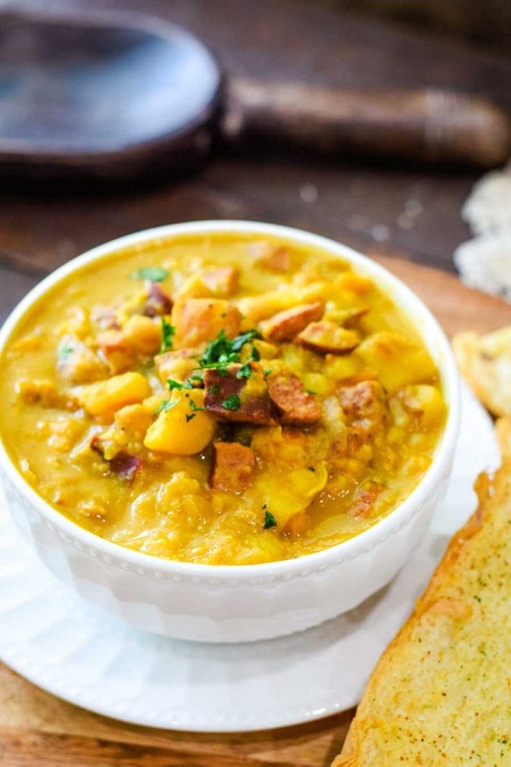 Spanish Bean Soup in a white bowl with a slice of buttery garlic bread.