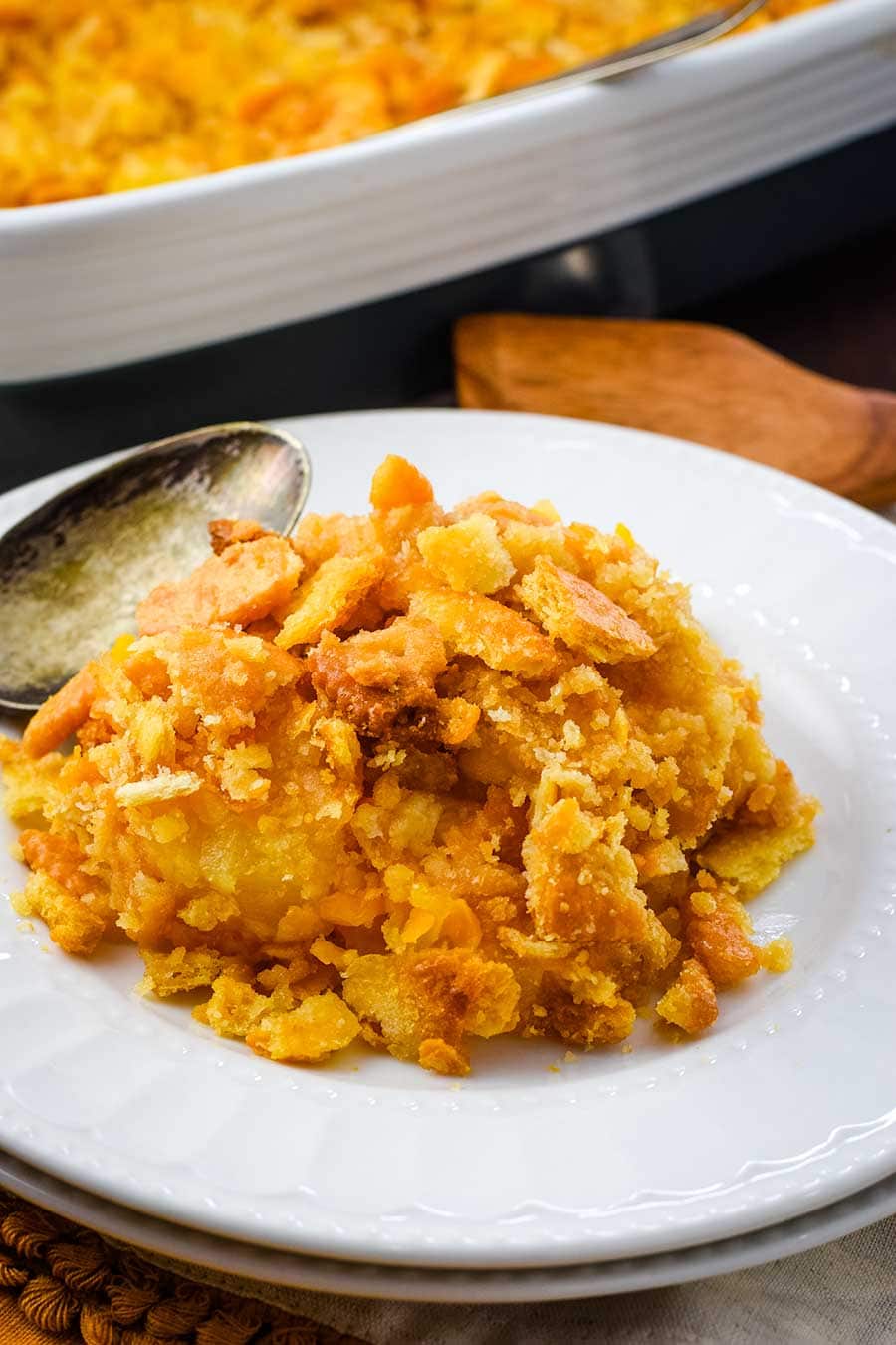 A scoop of pineapple casserole on a white plate with a vintage serving spoon.