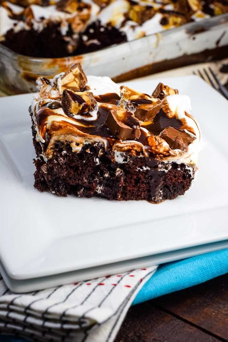 Slice of Snickers Poke Cake with chocolate and caramel syrup drizzled on top