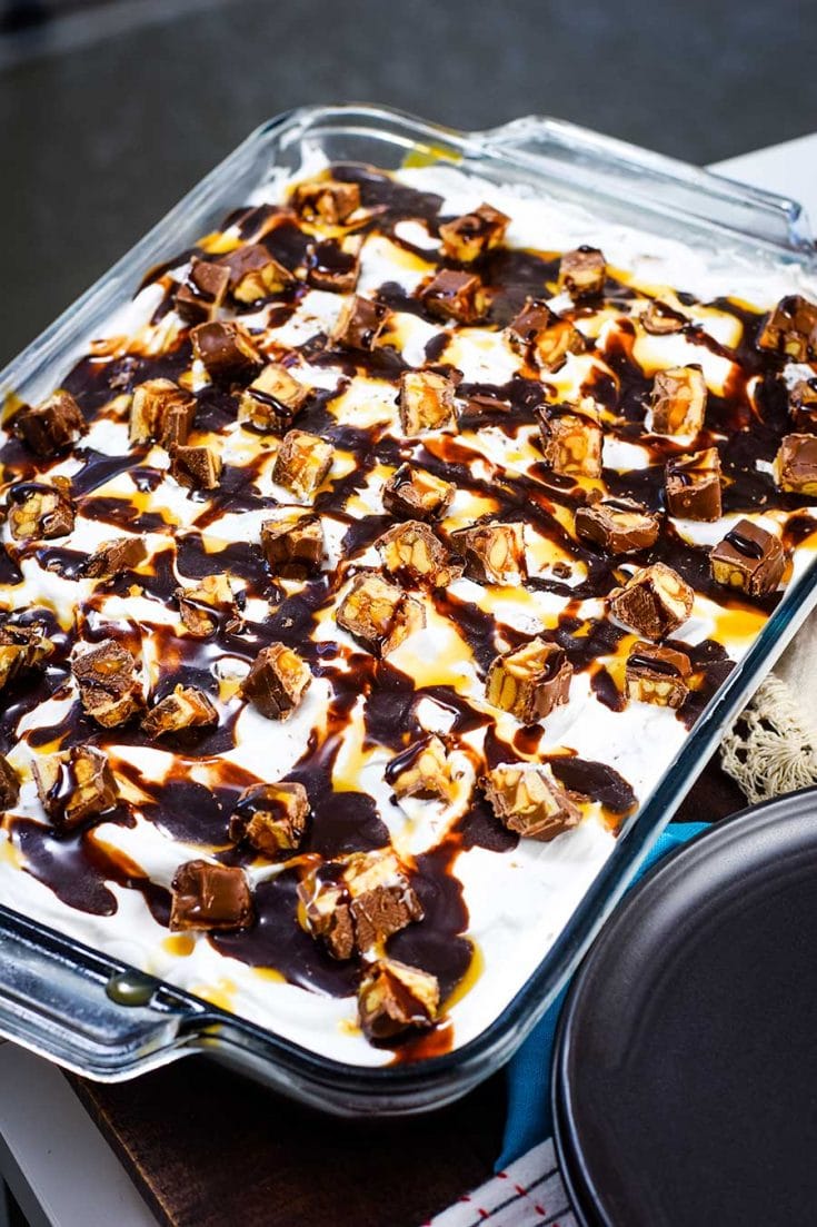 A large snickers poke cake on a baking dish.