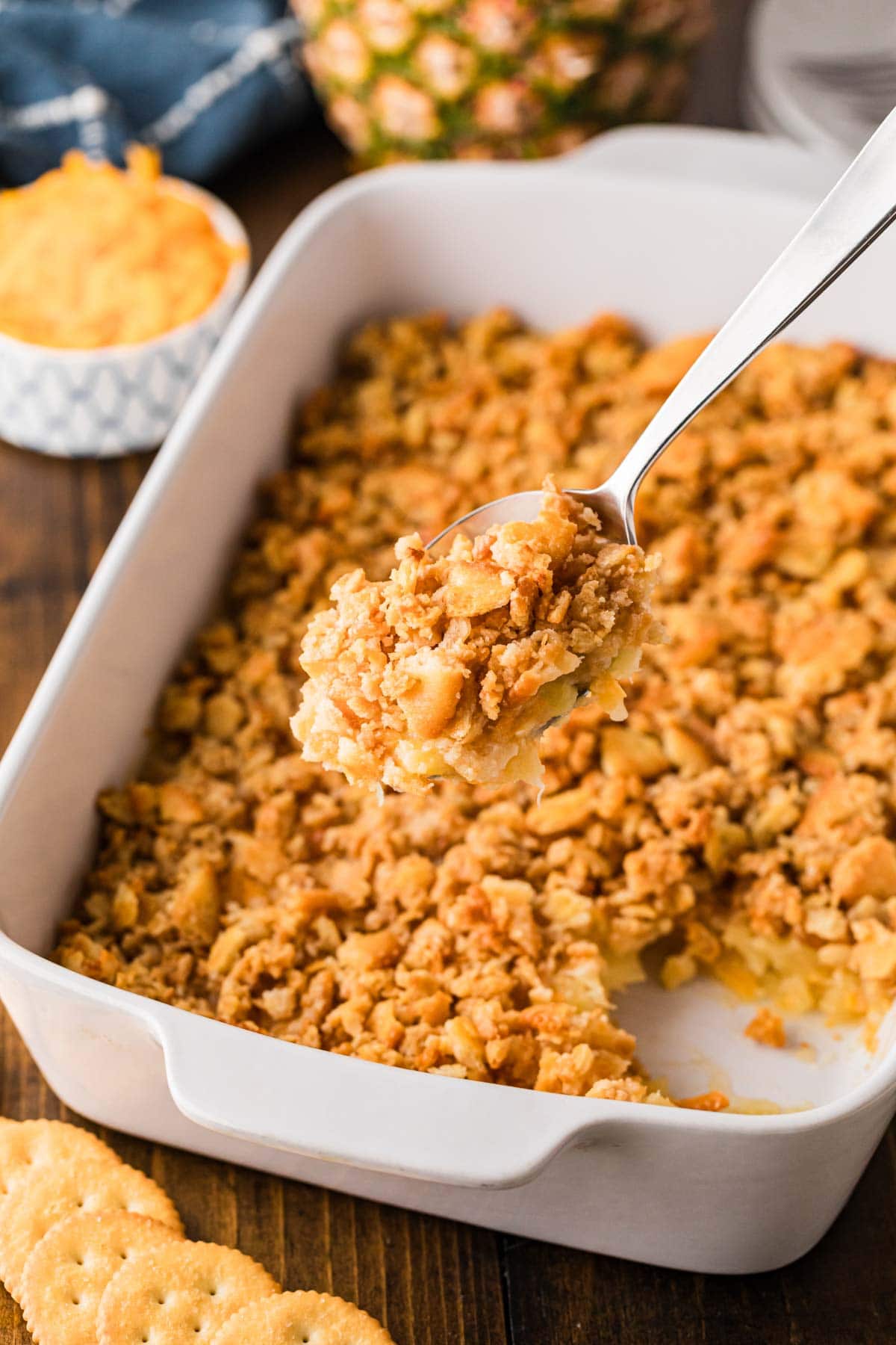 A serving spoon removing a scoop of pineapple casserole from a white baking dish.