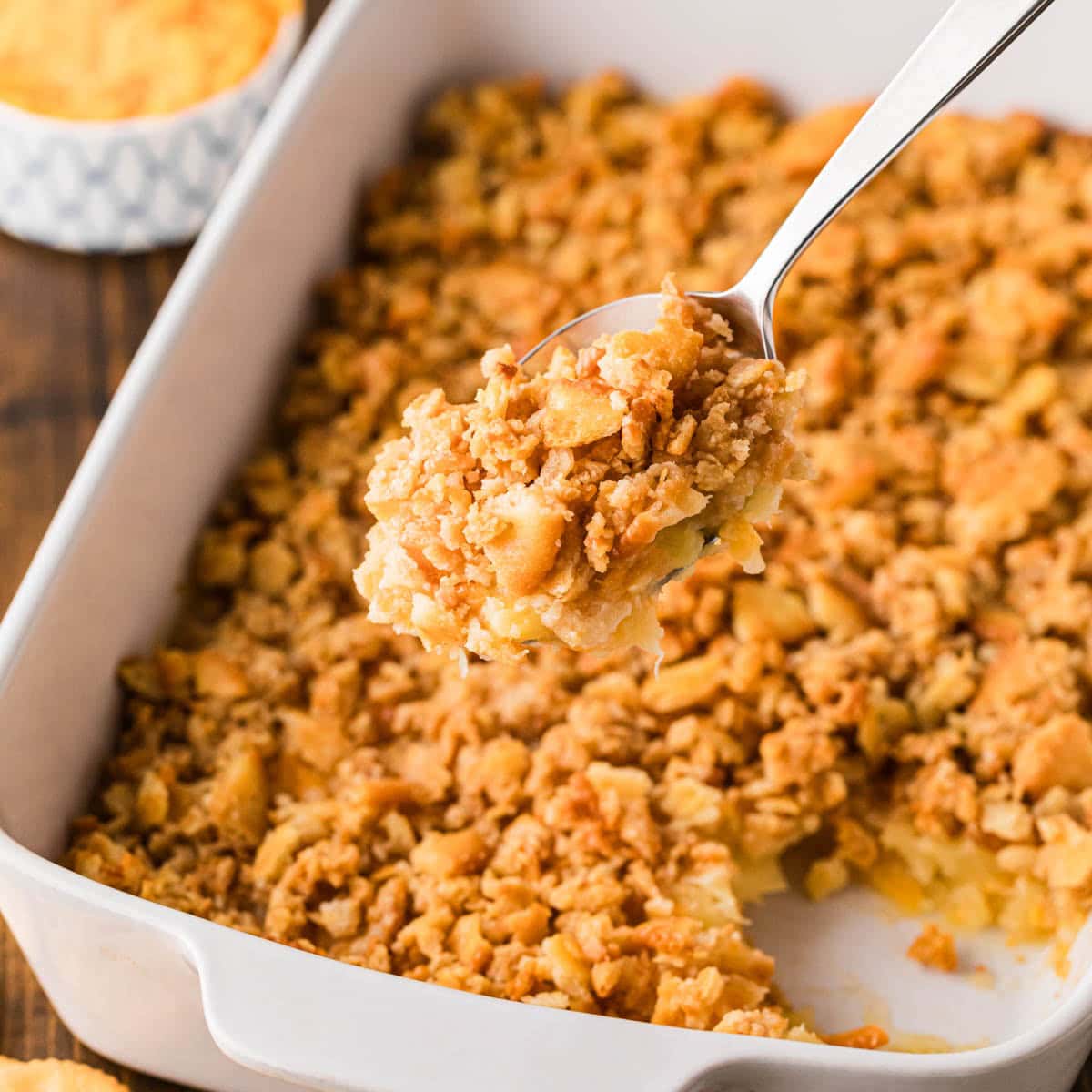 A serving spoon removing a scoop of pineapple casserole from a white baking dish.