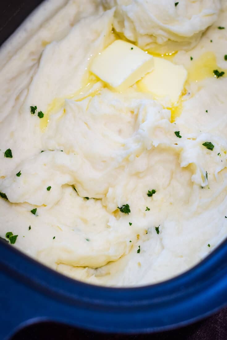 Whipped slow cooker mashed potatoes with two pats of butter on top sprinkled with parsley.