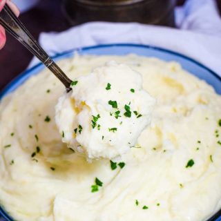 A bowl of slow cooker mashed potatoes served with a spoon.