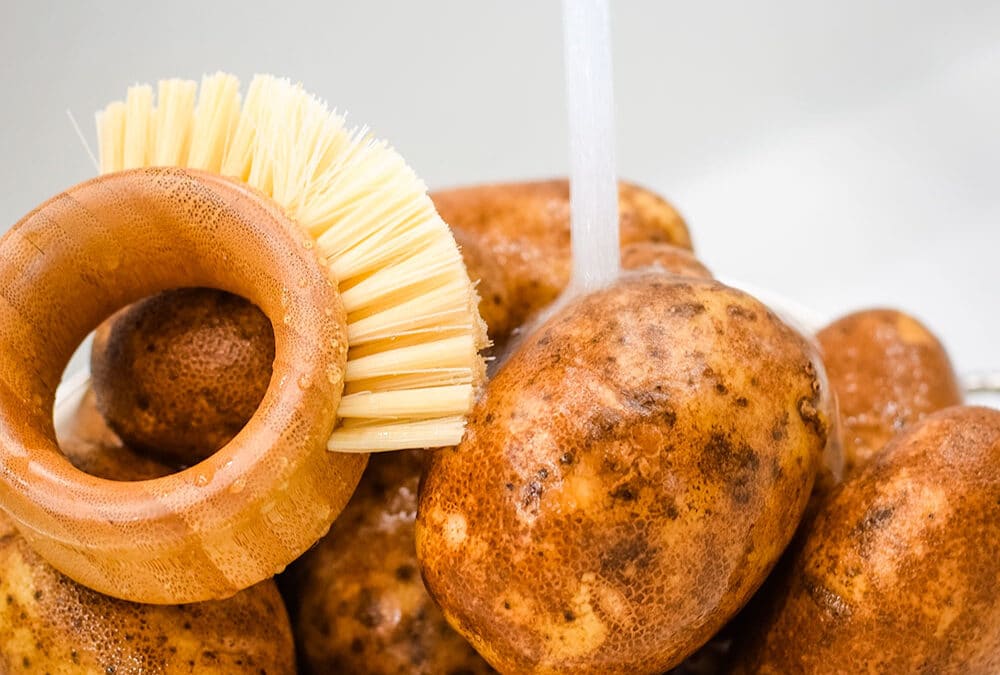 Image of russets potatoes being rinsed with a scrub brush close by.