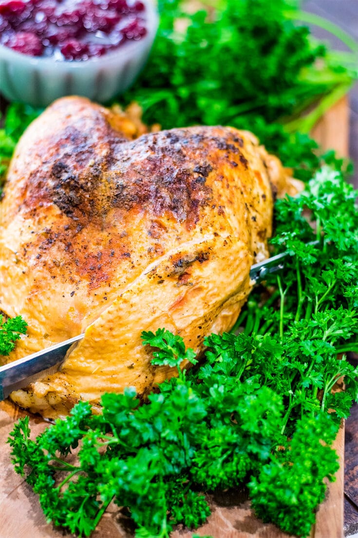 Turkey on a wooden platter being cut with an electric knife.