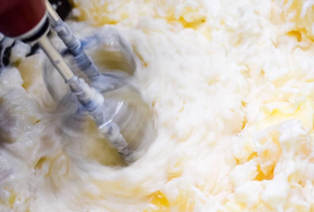 Cooked potatoes being mixed with a hand mixer.