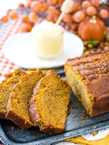 A close up of the Best Pumpkin Bread Recipe in both slices and as a loaf with softened butter in the background