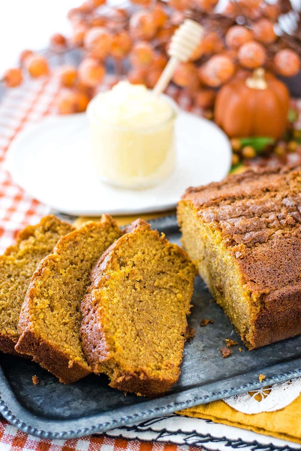 A close up of the Best Pumpkin Bread Recipe in both slices and as a loaf with softened butter in the background