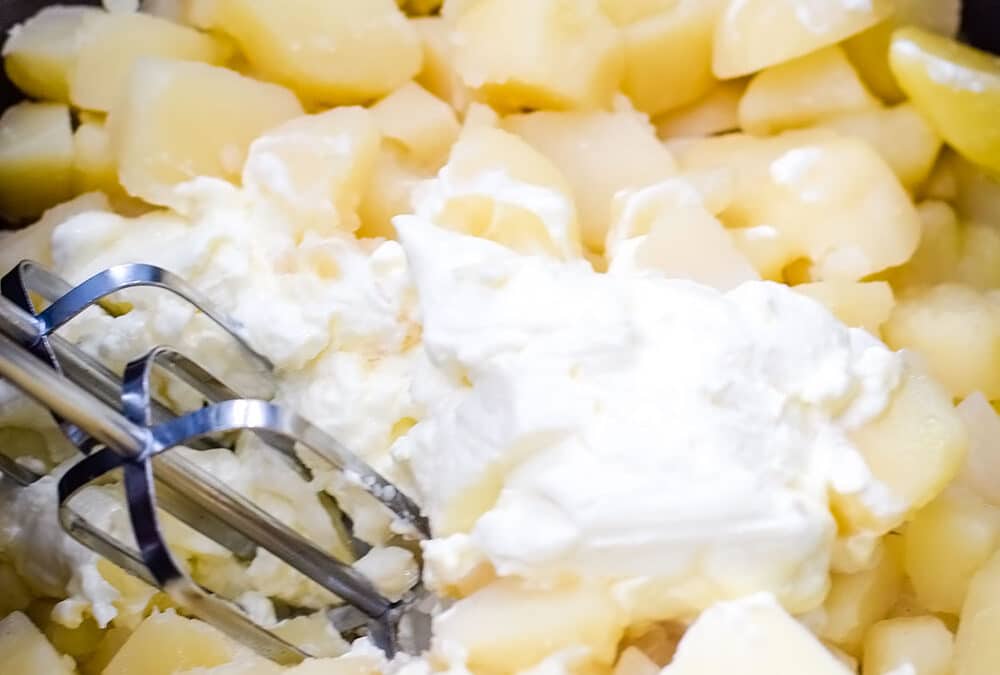 Cooked cubed potatoes with cream cheese about to be mixed with a hand mixer.