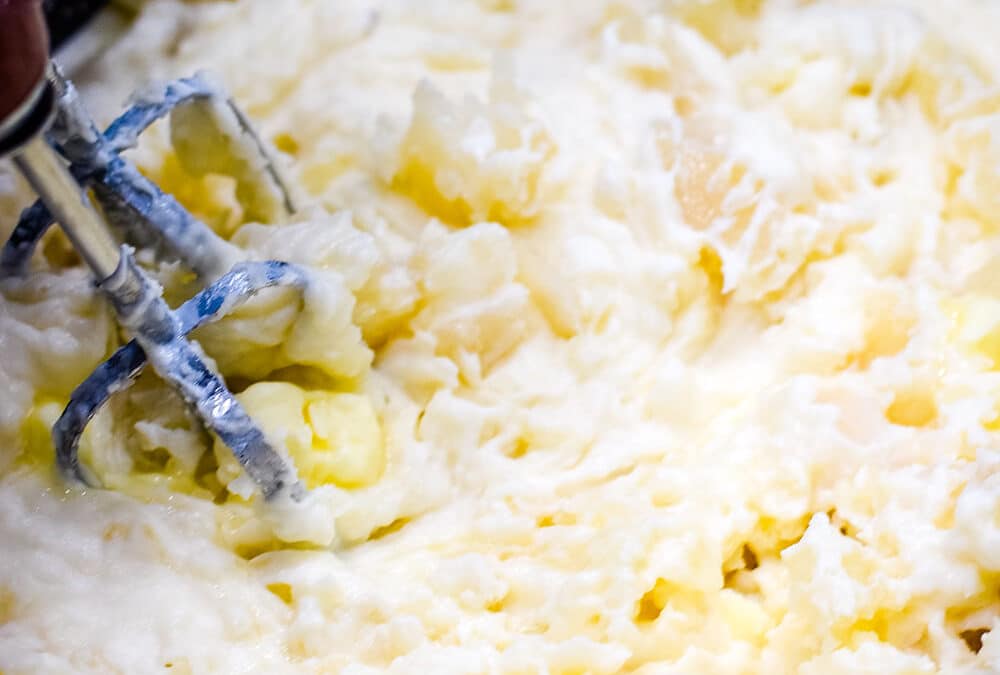 Cooked potatoes with butter added being mixed with a hand mixer.