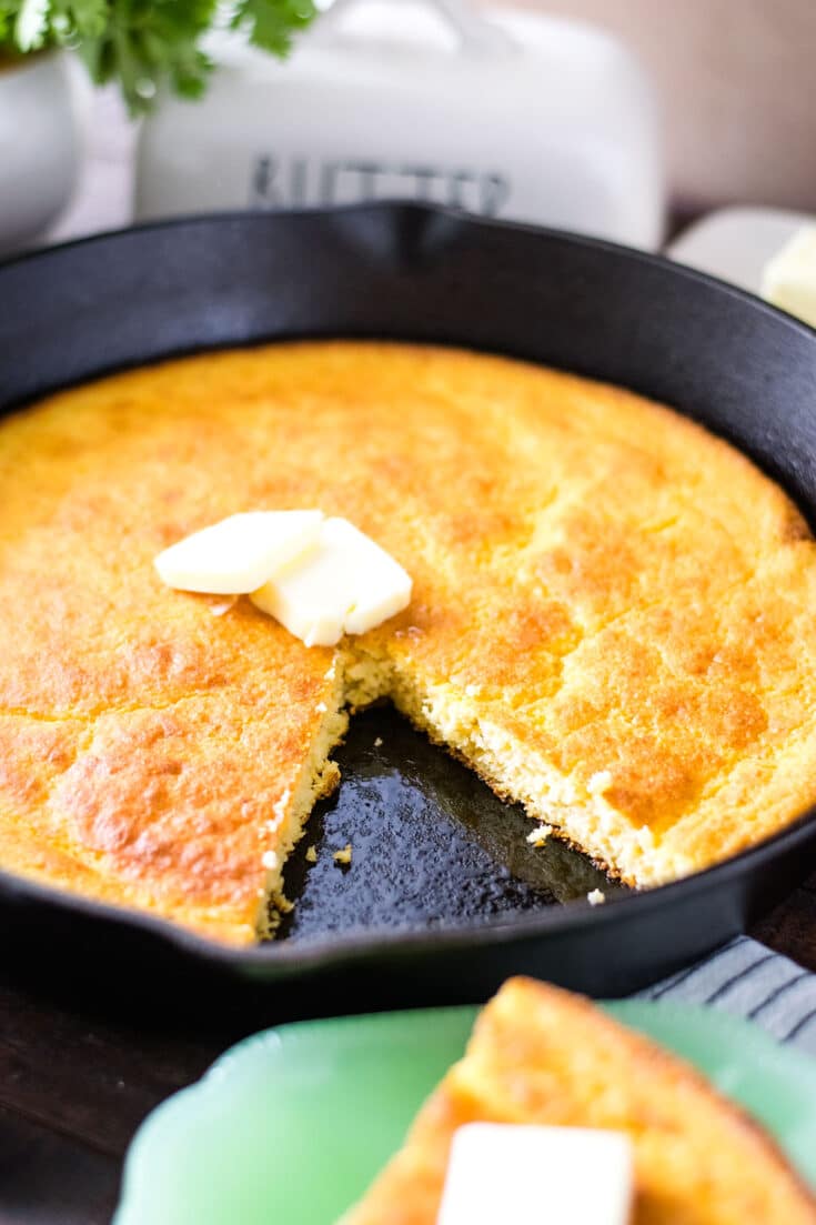 A close-up of cornbread with a slice removed and butter on the top.