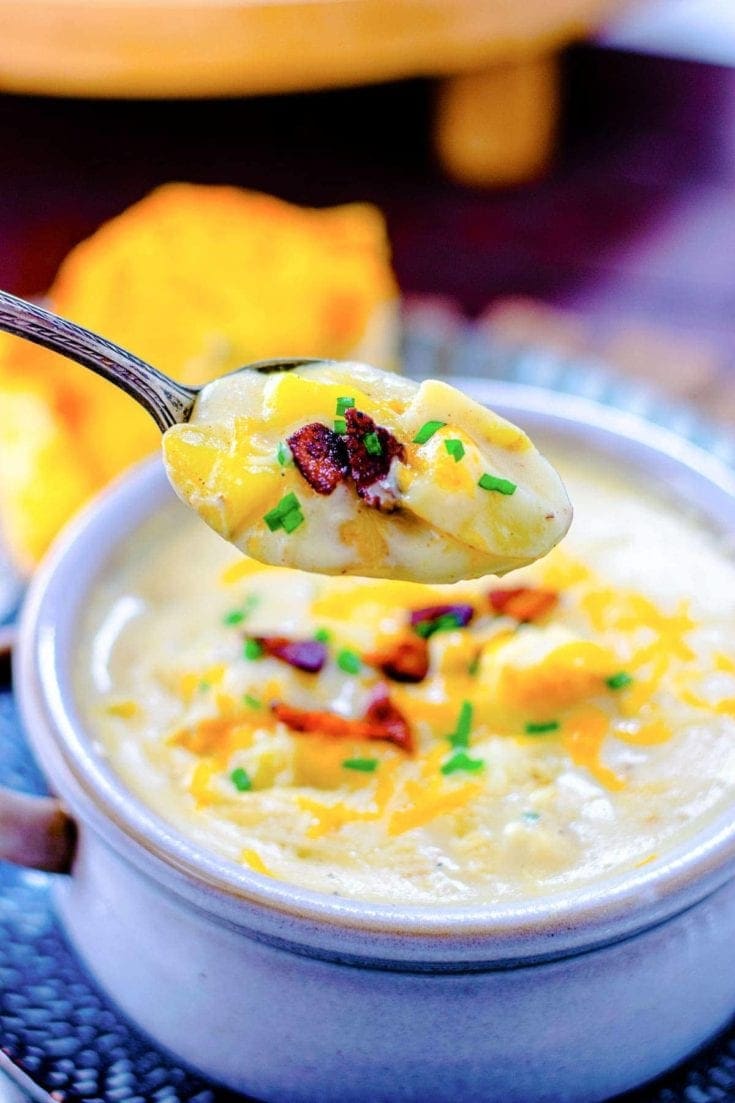 A bowl of creamy potato soup with garlic bread in the background. 