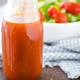 A close-up of a glass of Catalina salad dressing with a green salad and tomatoes in the background.