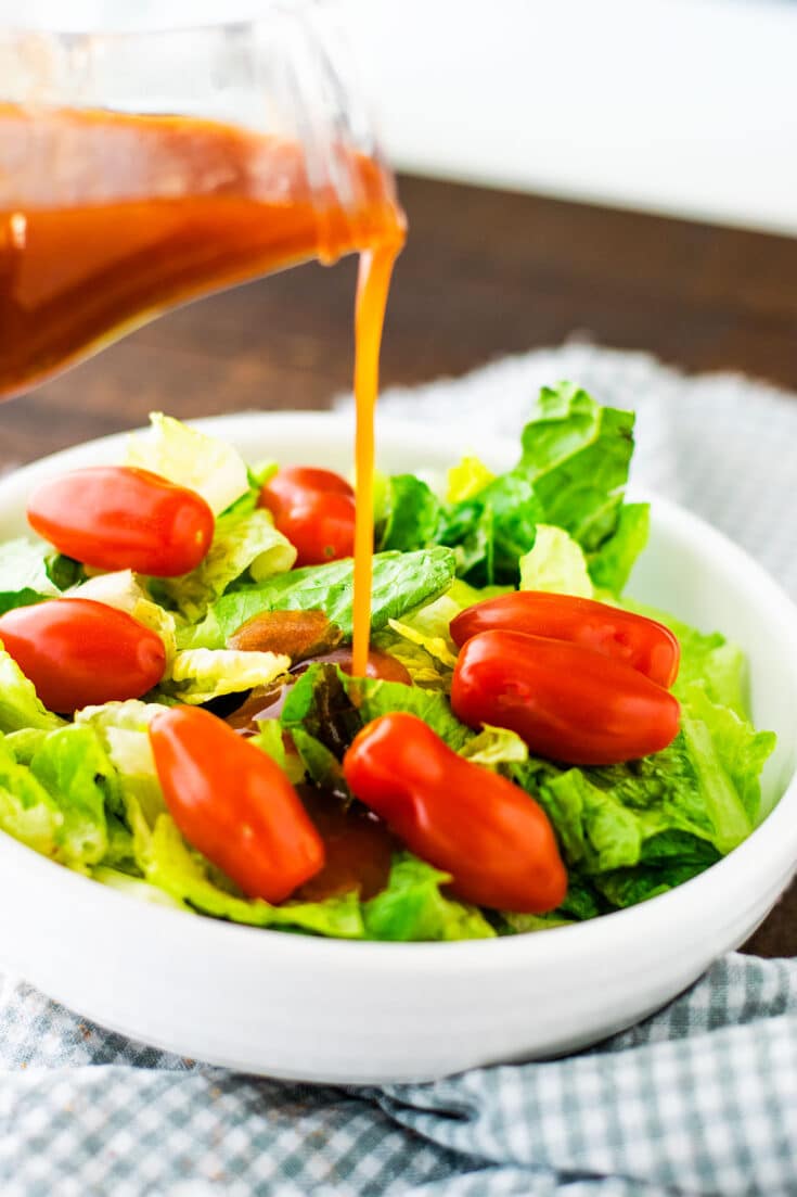 A green salad with tomatoes with Catalina dressing being poured over the top.