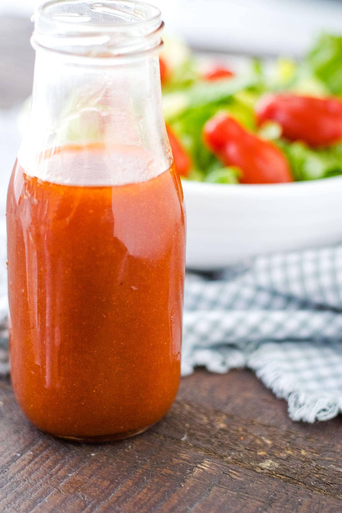 A close-up of a glass of Catalina salad dressing with a green salad and tomatoes in the background.