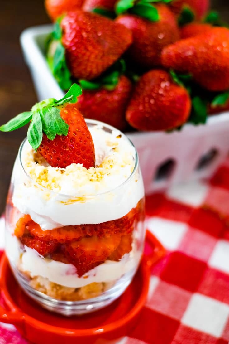 No Bake Strawberry Cheesecake Parfait on a red crock with strawberries in the background.
