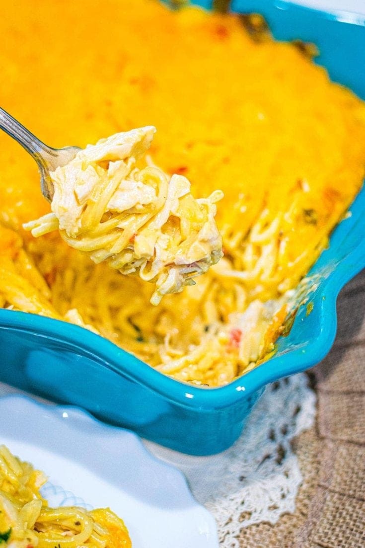 A fork filled with swirled baked chicken spaghetti with casserole beneath it.