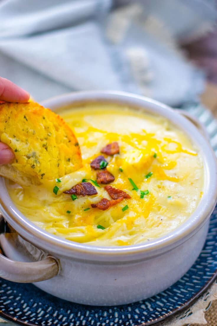 A bowl of potato soup with a slice of garlic bread being dipped into it.